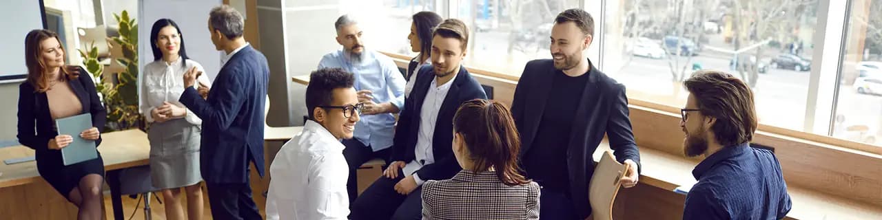 Diverse persone conversano in un ufficio luminoso; alcune sedute, altre appoggiate a un tavolo.